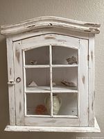 Full view of the wall mounted shabby chic cabinet with glass front showing shelves with vase and seashells inside