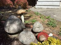 Group photo showing five mushroom sculptures in various sizes, textures resembling stone or concrete, colors including grey, red with white spots, and gold.