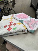 Two handmade vintage quilts folded side by side on a table showing overall size and colors.