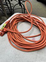 Coiled orange extension cord about 50 feet long on table showing both ends of the cord.