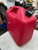 Red 5.5 gallon gas can, showing handle and black screw-on cap at an angle.