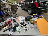 Overview of a variety of adding machines, calculators, staplers, and office supplies arranged on a gray table