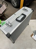 Side angle of a silver vintage metal case showing black plastic handle, metal latches and reinforced corners with some signs of wear.