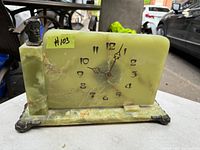 Full front view of green onyx Art Deco clock showing clock face with black Arabic numerals and ornate bronze hour/minute hands. Left column includes a bronze bust of a man's head.