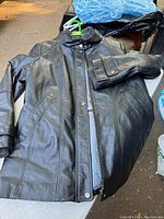 Front view of black men's Danier leather coat laid flat, showing snap-button collar and two side pockets.