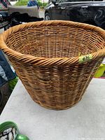 Large handwoven wicker basket placed on a table outdoors, showing weave details and size perspective with other objects nearby.