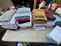 Wide shot of multiple folded towels stacked on a folding table outdoors, showcasing various colors and types of towels.