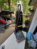 Front view of Bissell ProHeat 2X carpet shampoo cleaner showing the overall unit with transparent water tank, black handle with attached hose, and yellow foot pedal.