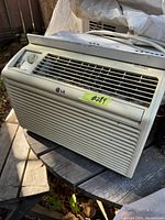 Front and angle view of LG window air conditioner with control knob and vent grille, unit resting on outdoor table surface