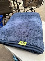 Folded navy blue weighted blanket showing textured sherpa/fleece side with square pattern stitching, placed on outdoor surface.