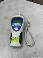 Photo showing front view of Welch Allyn SureTemp Plus digital thermometer with coiled probe cable and control buttons on a light workbench surface.
