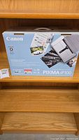 Canon PIXMA iP100 printer box on wooden shelf, showing front of box with printer image and branding.