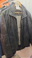 Front view of Danier black leather jacket hanging on a hanger with zipper closure and two zippered pockets visible.