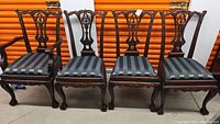 Full view of all four wooden dining chairs with carved details, claw & ball feet, and striped upholstered seats.