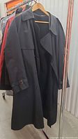 Black Harry Rossen overcoat hanging on a rack, showing front and length, including sleeve with buckle cuff detail.
