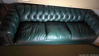 Front view of the forest green leather tufted sofa showing seat cushions and tufted backrest.