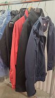 Five assorted men's coats hanging on a rack, showing different colors and styles.