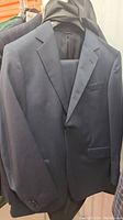 Front view of men's suit jacket in dark color hanging on a rack