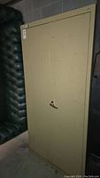 Front view of beige metal cabinet with closed two doors and handle with lock on right door.
