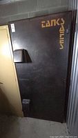 Front view of a large black metal safe with orange stencil text 'TANKS SAFES' and two protruding lock plates.