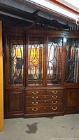 Full view of a large Thomasville hutch with glass doors, multiple drawers, carved wood details, and a glossy finish.