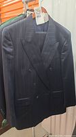 Front view of navy blue Yves Saint Laurent pinstripe suit jacket on hanger, showing double-breasted peak lapels and button closure.