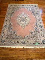 Full view of the rectangular pink decorative area rug with central medallion and ornate border.