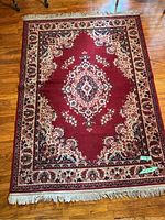 Full view of the red and ivory traditional style area rug with a central medallion pattern and fringed borders on hardwood floor.
