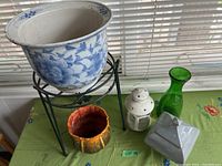 Wide view showing all items in the lot including a blue and white ceramic pot on plant stand, orange pot, white lantern, green vase, and gray planter on table by window
