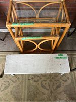 Two stacked bamboo nesting tables with glass tops and a white wooden bench in front on a patterned rug.