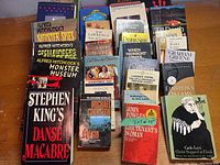 Photo of assorted books including titles by Stephen King, Alfred Hitchcock, Michael Crichton, and classic literature authors arranged on a wooden surface.