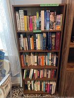 Front view of wooden bookshelf filled with various books showing spine titles and general appearance of lot
