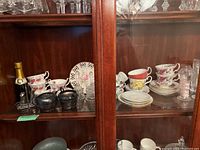 Photo of china cups, saucers, plates, sterling silver salt and pepper shakers, miniature champagne bottle on display shelf