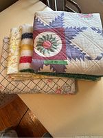 Photo showing a stack of five comforters and blankets with various patterns and colors suitable for double/full bed.