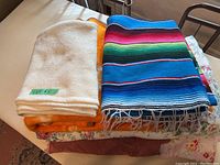 Photo showing cream fleece blanket, orange floral blanket, colorful striped serape-style blanket stacked on bed.