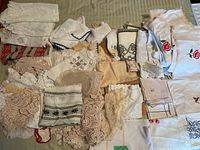 Wide view of assorted doilies and decorative linens on a beige surface showing variety of lace, crochet, and embroidered pieces folded and spread out