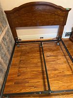 Wooden headboard mounted on metal bed frame rails, showing curved top and decorative detail.