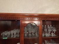 Wide view of cut crystal glasses displayed in wooden cabinet showing multiple glass sizes and styles