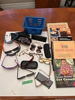 Top view showing assortment of retro sunglasses, eyeglasses, cases, and three books including one gardening book and two cookbooks on wooden table.