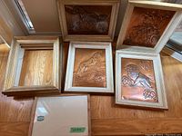 Six pieces arranged on floor: four copper embossed art pieces with horse and nature themes, two empty decorative wooden frames, and one empty framed glass panel with label.