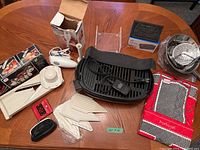 Full lot on wooden table showing the various kitchen appliances, mandolin attachments, bacon press, apron, and wallets.