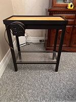 Metal aquarium stand showing the black metal frame with wooden top surface, electrical outlet on side with power cable, and lower glass shelf.