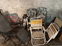 9 outdoor chairs grouped including 2 black mesh zero gravity reclining lounge chairs, 2 floral fabric folding chairs, 2 white metal floral cushioned chairs, and 3 white metal chairs with yellow and white plastic slats.