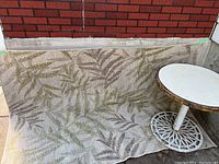 Outdoor carpet with a beige base and green/brown leaf pattern hanging over a ledge showing full pattern and texture.