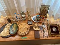 Photo showing entire lot on a wooden table including figurines, plaques, plates, rosaries, candles, framed art and icons.