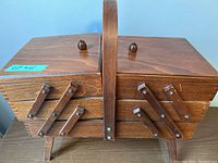 Closed view of vintage expandable wooden sewing kit with carry handle and wooden knobs.