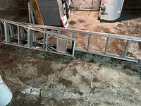 Photo showing the 10-foot aluminum ladder laid flat on concrete basement floor, displaying rectangular rungs and side rails.