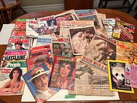 Wide view of vintage magazines and newspapers spread on table. Titles include Chatelaine, Canadian Living, Cracked, Starweek, People, National Geographic and 1982 Royal Wedding newspapers.