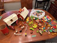 Overview of vintage Fisher Price Little People playsets including barn, silo, schoolhouse, and various figures and accessories spread on a table.