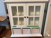 Front view of the white wall-mounted bathroom cabinet showing two glass paneled doors and three white woven baskets below